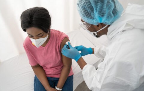 Doctor cleaning skin on female patient's arm with disinfectant before injection